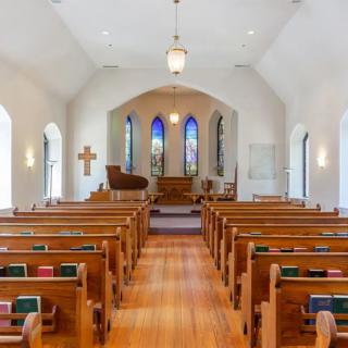 Interior view of a church with wooden pews and stained glass windows.