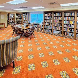 A cozy library with wooden bookshelves and an orange carpeted floor, featuring a central reading area.