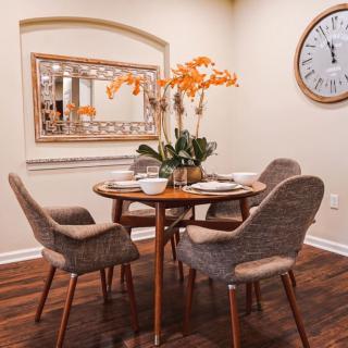 A cozy dining area with a wooden table and four cushioned chairs, adorned with vibrant orange flowers and surrounded by stylish decor.