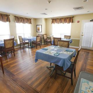 A neatly arranged dining area with several tables and chairs, featuring wooden floors and natural light from windows.