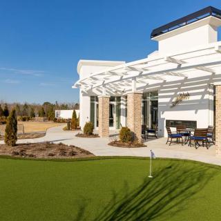A modern house with a backyard patio and putting green on a sunny day.