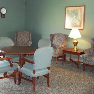 A cozy living room with several chairs, a table, a lamp, and a painting on the wall.