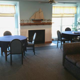 A cozy living room with tables and chairs arranged around a fireplace, decorated with a model ship on the mantel.