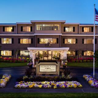 A well-lit hotel building at night with a flag and flower arrangements in the foreground.