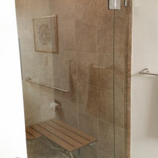 A modern glass shower space featuring a wooden bench and elegant tilework.