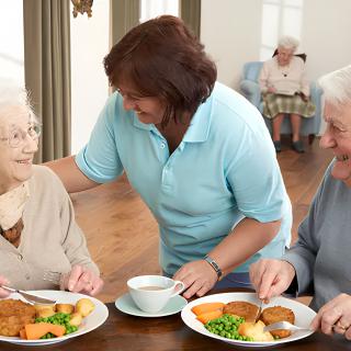 A caregiver assists elderly individuals during meal time in a nursing home environment.