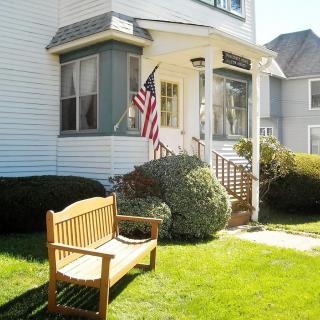 A quaint suburban house with an American flag displayed on the front porch and a wooden bench on the lawn.