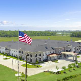 A large building with an American flag flying in front, surrounded by a parking lot and greenery.