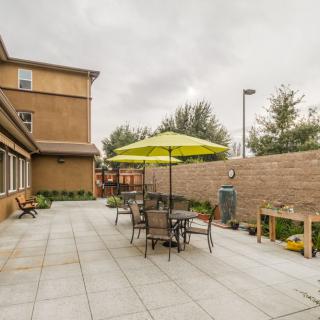 A patio area with tables, chairs, and an umbrella set against a brick wall.