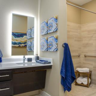 A modern bathroom with illuminated mirror, blue towels, and abstract artwork on the walls.