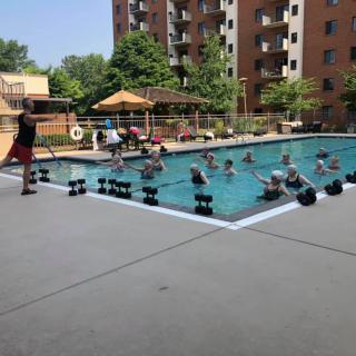 A group of people participating in a water aerobics class at an outdoor swimming pool.