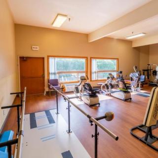 A therapy room equipped with various exercise equipment and parallel bars, designed for rehabilitation exercises.