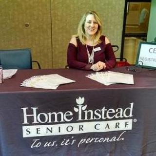 A representative from Home Instead Senior Care at an informational event, ready to assist with inquiries about senior care services.
