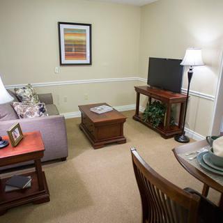 A cozy living room with a sofa, coffee table, TV stand, and a small dining area.