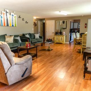 A spacious living room with wood flooring, featuring comfortable couches, a recliner, and modern wall art.