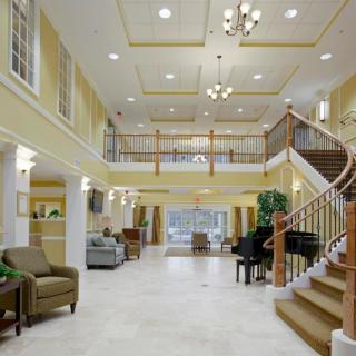 A spacious and elegant lobby with a grand staircase, seating area, and a piano.