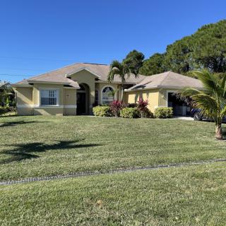 A single-story house with a well-maintained lawn and palm trees under a clear blue sky.