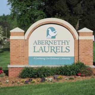 Entrance sign for Abernethy Laurels featuring a brick structure surrounded by landscaped greenery.