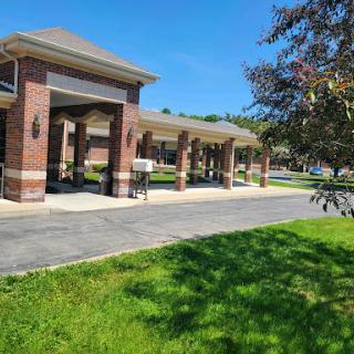 A well-structured building featuring a covered entryway, surrounded by lush green grass under a clear blue sky.