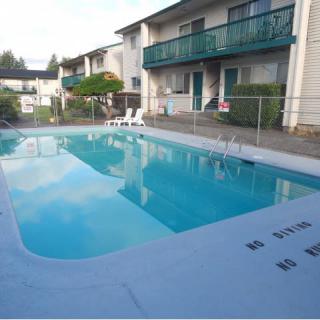 An outdoor swimming pool at an apartment complex with surrounding fence and deck chairs.
