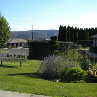 Scenic view of a building with a sign reading 'Chandler House' surrounded by lush greenery and hills in the background.