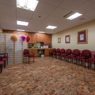 A spacious waiting room with multiple chairs arranged along the walls, featuring warm lighting and decorative elements.