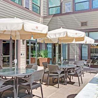 An outdoor patio area with tables, chairs, and umbrellas next to a building with large windows.