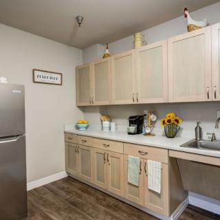 A modern kitchen with light wooden cabinets, a sleek refrigerator, and a countertop featuring a coffee maker and sunflowers.