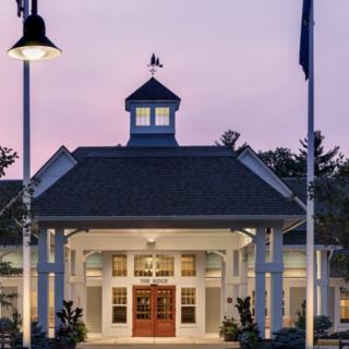 A well-lit building entrance at dusk, featuring a cupola and flanked by two flags.