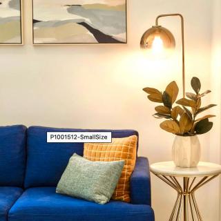 A cozy living room setup featuring a blue sofa with decorative cushions, a sleek floor lamp, indoor plant on a side table, and wall art.