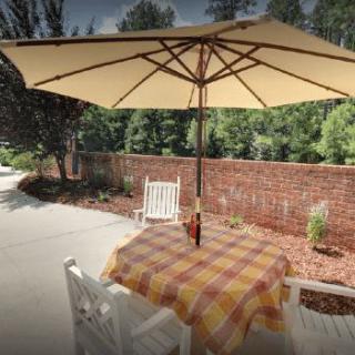 A cozy outdoor patio with a table, chairs, and a large umbrella, set against a brick wall and garden backdrop.
