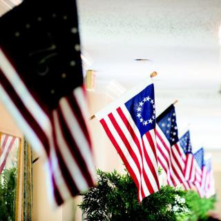 A row of American flags, including the historic Betsy Ross flag, displayed indoors.