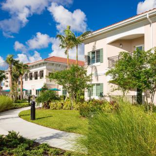A tropical residential building surrounded by lush landscaping and palm trees under a bright blue sky.