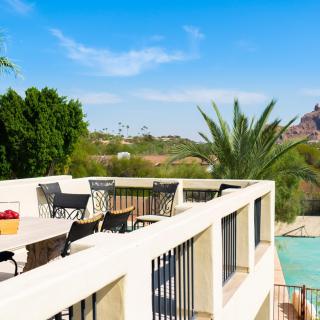 A sunny terrace with outdoor furniture overlooking a pool and palm trees in a picturesque landscape.
