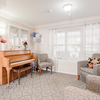 A cozy living room with a piano, comfortable chairs, and bright natural light.