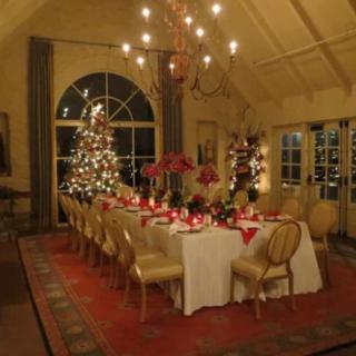 A beautifully decorated dining room for Christmas, featuring a long table set with festive decor and illuminated by warm lights.