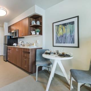 A modern kitchen with wood cabinets, featuring a cozy dining area with a round table and chairs, complemented by artwork on the wall.