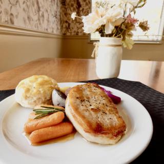 A plate of grilled chicken served with carrots and a bread roll on a dining table.