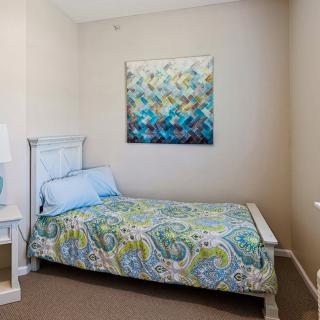 A cozy bedroom with a colorful quilt and abstract artwork above the bed.