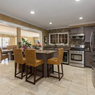 A modern kitchen with a central island, dining area, and stainless steel appliances.
