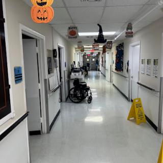 A hospital hallway adorned with Halloween decorations, featuring a wheelchair and a caution sign on the floor.