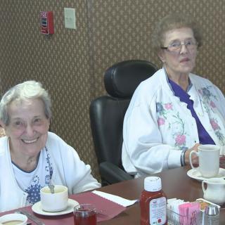 Two elderly women enjoying their time over tea and coffee at a dining table.
