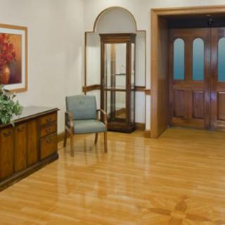 A quiet lobby area with a wooden floor, featuring a chair, a side table, and a revolving door.