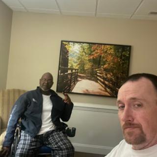 A friendly selfie shared between two individuals, one in a wheelchair, enjoying time together indoors.