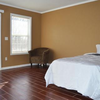 A spacious bedroom with hardwood flooring, featuring a bed, chair, and large window.
