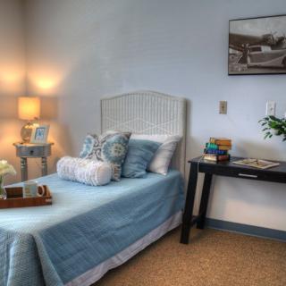 A cozy bedroom with a neatly made blue bed, soft pillows, ambient lighting, and tasteful decor.