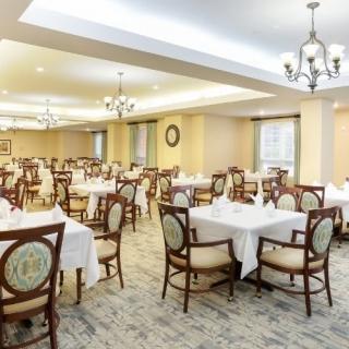 A well-lit dining area with elegantly arranged tables and chairs, featuring chandeliers and classic decor.