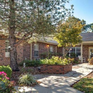 A well-maintained brick house with a landscaped front garden and a walkway surrounded by trees.