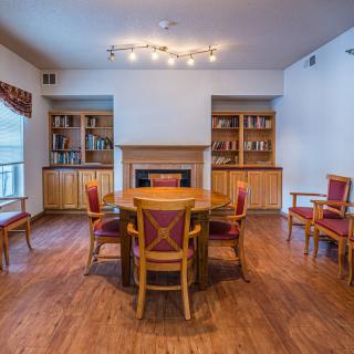 A cozy living room with a round wooden table surrounded by chairs, flanked by bookshelves and a fireplace.