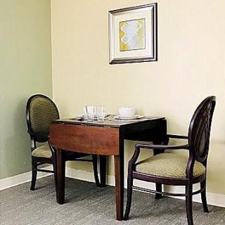 A small dining area with a wooden table and two upholstered chairs, adorned with a framed artwork on the wall.